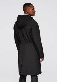 Abrigo negro con capucha y cintura ceñida, de textura suave y detalles en los puños con botones. Presenta un corte largo y recto, con un diseño minimalista.