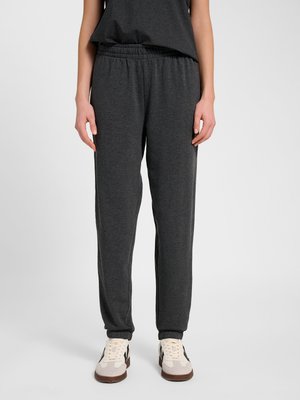 Osoba nosząca ciemnoszare spodnie dresowe z elastyczną talią i mankietami, połączone z jasnymi butami sportowymi z brązowymi podeszwami.