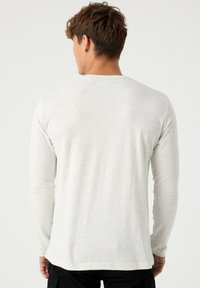 Camisa de manga larga en gris claro, hecha de un material suave, con un diseño sencillo, cuello redondo y corte recto, sin patrones visibles.