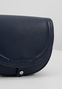 Granatowa skórzana torebka z zakrzywioną klapką, teksturowanym wykończeniem, zapięciem na zatrzask oraz tłoczonym logo marki z przodu.