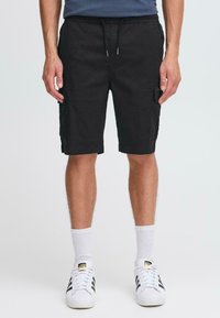 Shorts cargo noirs avec une taille à cordon de serrage, des poches latérales et un tissu légèrement texturé. Associés à des chaussettes blanches et des baskets à rayures noires.