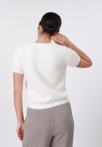 Pull blanc à manches courtes avec une texture douce et duveteuse, doté d'un col rond et d'une coupe ajustée, associé à un pantalon à motif à carreaux.