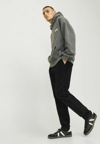 Gray hoodie with front pocket, black corduroy pants, and black sneakers featuring white accents. Model stands in profile against a light background.
