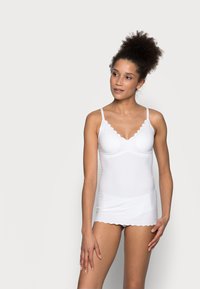 White camisole featuring a scalloped neckline, thin adjustable straps, and a soft texture, designed for comfort and fit.