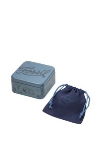 Scatola metallica quadrata di colore azzurro chiaro con una grafica e la scritta "Fossil" sul coperchio accanto a un sacchetto di stoffa blu scuro con coulisse.
