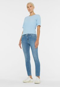 Blue and white striped short-sleeve top with scalloped hem paired with light blue skinny jeans and white sneakers. Simple, casual outfit.