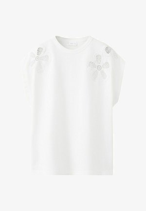 Bela kratka majica s kratkimi rokavi in okroglim izrezom, okrašena z dvema velikima cvetličnima čipkastima aplikacijama na ramenih.