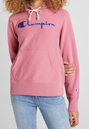 Felpa rosa con cappuccio regolabile, tasca frontale a marsupio e logo "Champion" ricamato in blu. Tessuto morbido con polsini e orlo a coste.