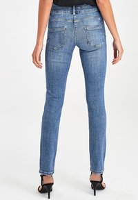 Jeans ajustados de denim azul con cinco bolsillos, ligeras arrugas y dobladillo enrollado. La tela tiene una textura suave y un desvanecimiento mínimo.
