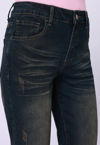 Jean en denim foncé avec une coupe slim, présentant des détails usés subtils, des coutures prononcées et un design classique à cinq poches.