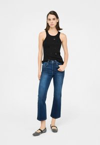 Top negro sin mangas con embellishments, jeans acampanados azules con dobladillo descolorido y bailarinas grises con estampado. Conjunto sencillo y casual.