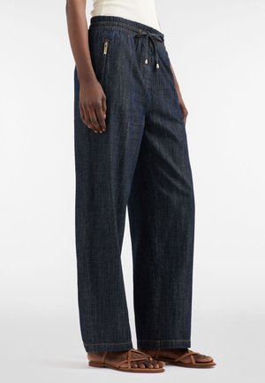 Pantaloni in denim scuro a gamba larga con vita elasticizzata e coulisse. Caratterizzati da tasche con zip e dettagli di cuciture a contrasto.