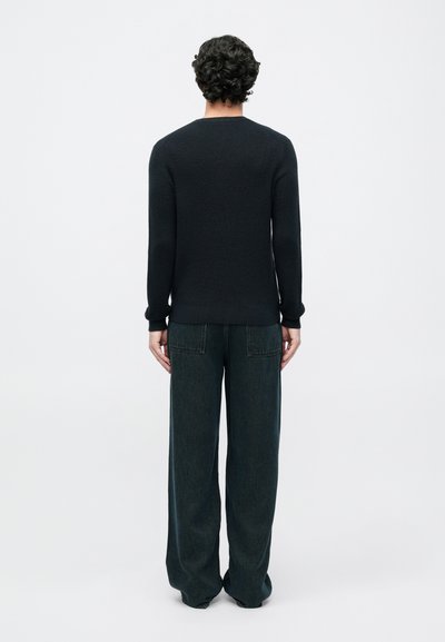 Suéter oscuro de canalé con mangas largas, combinado con pantalones de denim oscuro de pierna recta y holgados. Diseño simple y minimalista.