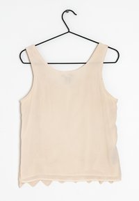 Top senza maniche beige realizzato in tessuto leggero, con orlo ondulato nella parte inferiore e una superficie liscia. Appeso a un gancio nero.