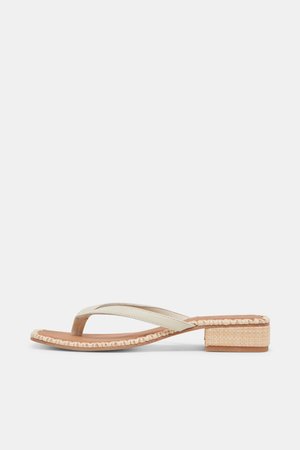 Beige sandal med lav hæl og vævet kant rundt om sålen samt en rem med tåadskillelse mod en hvid baggrund.