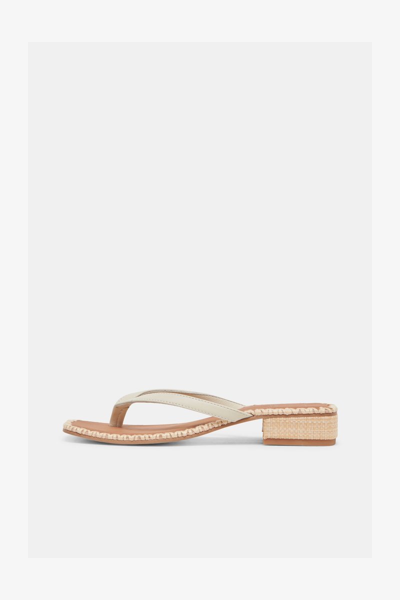 Μπεζ σανδάλι με χαμηλό τακούνι, διακοσμημένο με πλεκτό περίγραμμα γύρω από τη σόλα και σχέδιο με λουράκι ανάμεσα στα δάχτυλα, σε λευκό φόντο.