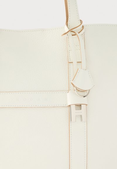 Λευκή δερμάτινη τσάντα χειρός με υφή στην επιφάνεια, διαθέτοντας επίπεδο λουράκι, ασημένια μεταλλικά στοιχεία και ανάγλυφο λογότυπο της μάρκας για μια καθαρή αισθητική.