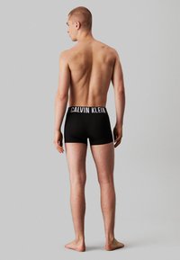 Sorte bomullsboxer med en hvit "CALVIN KLEIN" logo på midjebåndet, med en tettsittende design og jevn tekstur, vist fra bak.