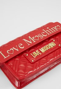 Pochette en cuir matelassé rouge avec marquage doré "Love Moschino" et ornements en forme de cœur sur le rabat et le panneau avant.