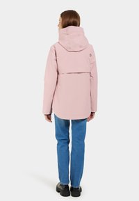 Ljusrosa vattentät jacka med huva, som har en vent bak och logotypdetalj. Kombineras med blå denim och svarta plattformsskor.