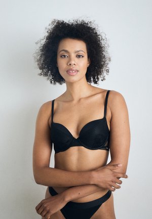 Zwarte onderbedekte bh met een gladde textuur, florale kanten accenten, verstelbare bandjes en bijpassende band, gecombineerd met een zwarte bikinionderkant.