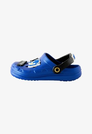 Clog albastru cu curea neagră reglabilă, decorat cu talismane cu personajul și logo-ul Sonic the Hedgehog.