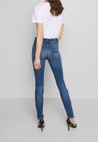 Jeans ajustados de color azul hechos de denim. Cuentan con cinco bolsillos, un leve desgaste y una cintura alta. Combinados con una camiseta blanca y tacones.