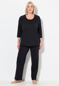 Conjunto de pijama negro que incluye una camiseta de manga tres cuartos con botón de cierre y detalles de encaje, combinado con pantalones holgados a juego.
