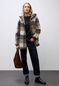 Kostkovaná vlna-měkká bunda v odstínech šedé, hnědé a krémové, se zapínáním na zip a kapucí. V kombinaci s tmavými džíny a černými kotníkovými botami.