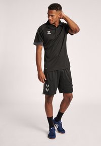 Sort athletic polo skjorte med korte ærmer, der har grå detaljer og logo; parret med sorte shorts og marineblå sko.