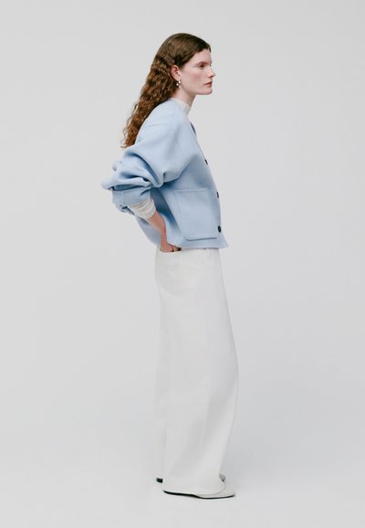 Lichtblauwe, geweven cardigan met een relaxte pasvorm, knopen aan de voorkant en zakken, gecombineerd met hoge witte wijde broek en zwarte schoenen.