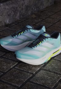 Light blue running shoes with white stripes, black accents, textured mesh upper, and yellow detail on the sole. Cushioned, sleek design.