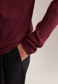 Camicia a maniche lunghe bordeaux con finitura testurizzata, polsini aderenti e vestibilità rilassata, abbinata a pantaloni neri con tasca laterale.