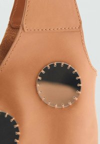 Borsa di pelle color tan con un accento a specchio metallico circolare, cucita con filo a contrasto e dalla texture morbida.