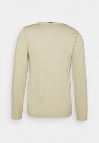 Beżowa koszulka z długim rękawem wykonana z miękkiego materiału, z zaokrąglonym dekoltem, prostym dołem i minimalistycznymi przeszyciami na rękawach.