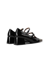Scarpe in vernice nera con tacco a blocco, caratterizzate da una punta affusolata e una punta di colore marrone a contrasto. Due dettagli a fascia con accenti circolari.