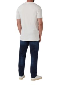 Kurzärmliges cremefarbenes Baumwoll-T-Shirt mit Rundhalsausschnitt, kombiniert mit dunkelblauen Jeans. Die Sneaker sind weiß mit einer strukturierten Sohle.