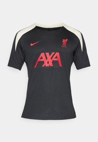 Maillot de football noir à manches courtes, présentant des accents beiges aux épaules. L'avant affiche le logo rouge "AXA" et le blason de Liverpool avec un contour rouge.