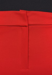 Rode rekbare stof tailleband met een gladde textuur, voorzien van een gevouwen rand en een subtiele naad. Het ontwerp is eenvoudig en minimalistisch.