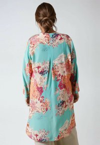 Tunique florale en turquoise, présentant un motif de fleurs multicolores vif. Manches longues et coupe droite avec un détail de pli dans le dos.