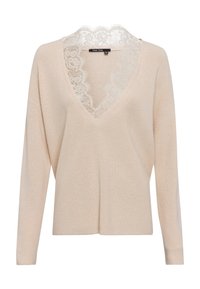 Pull beige en tricot avec un col en V et une bordure en dentelle au niveau du col. Comprend des manches longues et une coupe décontractée. Tissu texturé.