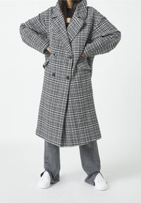 Harmaa-valkoinen ruudullinen takki, jossa kaksirivinen nappilista, suuret kaulukset ja sivutaskut, kerroksittain harmaiden farkkujen ja valkoisten tennarien päällä.