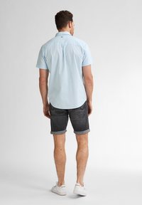 Cămașă scurtă, de culoare albastru deschis, cu guler standard, combinată cu pantaloni scurți gri închis, răsuciți, și adidași albi, văzută din spate.