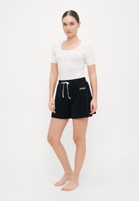 Svarta bomullsshorts med elastisk midja, vit dragsko och "HUGO"-logotyp på vänster fåll. Matchas med en figurnära vit topp.