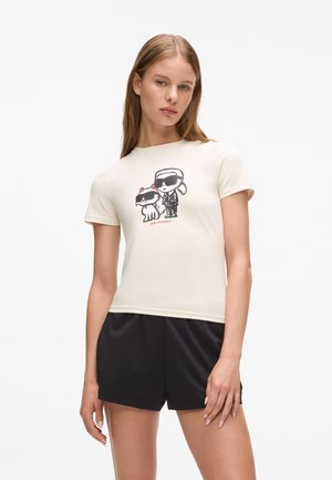 Short-sleeved cream t-shirt featuring a graphic of two cartoon characters in sunglasses, paired with black shorts. Smooth fabric texture.