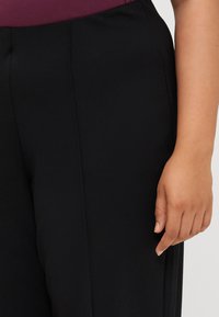 Close-up of a hand resting on black fabric, featuring tailored pants and a deep burgundy top. Emphasizes a stylish outfit and fabric texture.