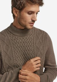 Sweter dziergany w stonowanym brązie z wysokim prążkowanym kołnierzem. Teksturowany wzór z warkoczami, diamentowymi kształtami i prążkowanymi mankietami.