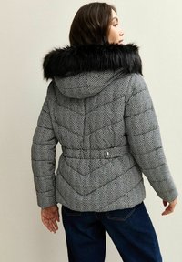 Kurtka puchowa pikowana w czarno-białym wzorze w jodełkę, z kapturem z sztucznego futra i detalami w postaci paska w talii.