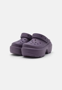 Sabots violets en mousse avec un design perforé, une sangle à l'arrière, une semelle surélevée et un fond texturé pour une meilleure adhérence.