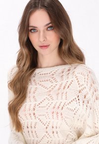 Crème-kleurige gebreide trui met een intricat openwerkt patroon, ronde halslijn en lange mouwen. Zachte en lichte textuur.